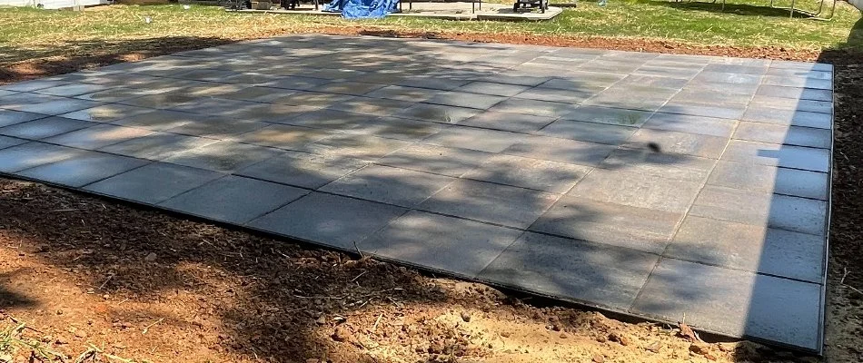 A patio in a backyard in Matthews, NC, with square concrete pavers.