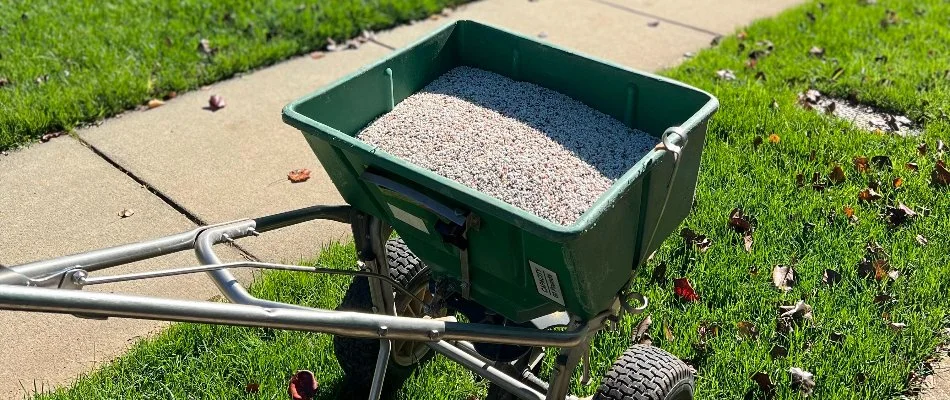 Granular fertilizer in green equipment on a lawn in Matthews, NC, near a sidewalk.